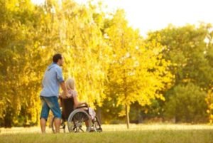 Man pushing woman in wheelchair through a park with Long Term Disability