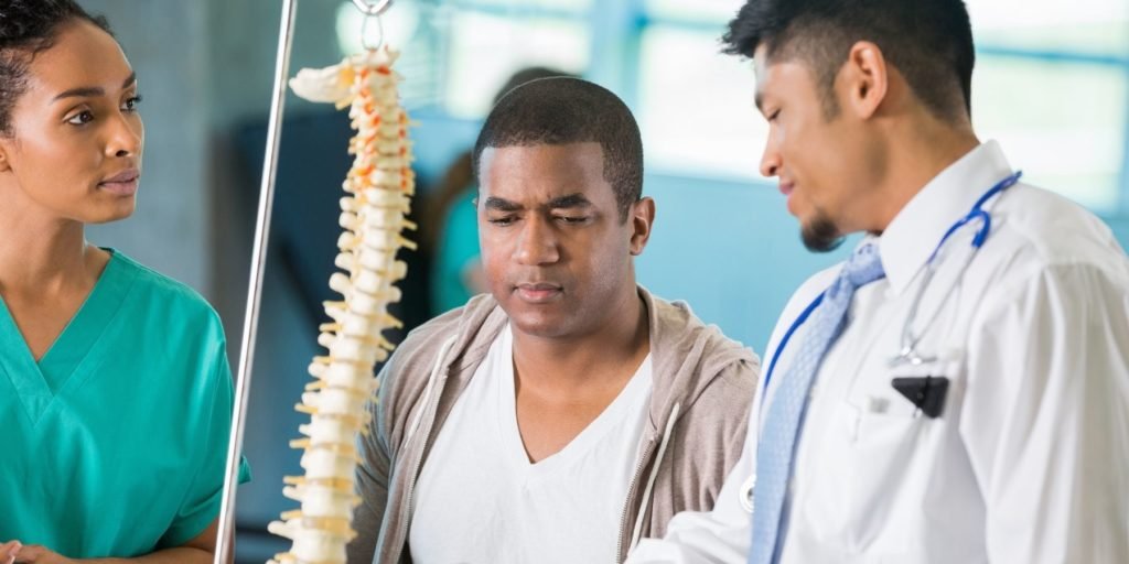 A young Asian man who recently suffered a spinal cord injury is speaking with his neurologist to discuss a treatment plan.